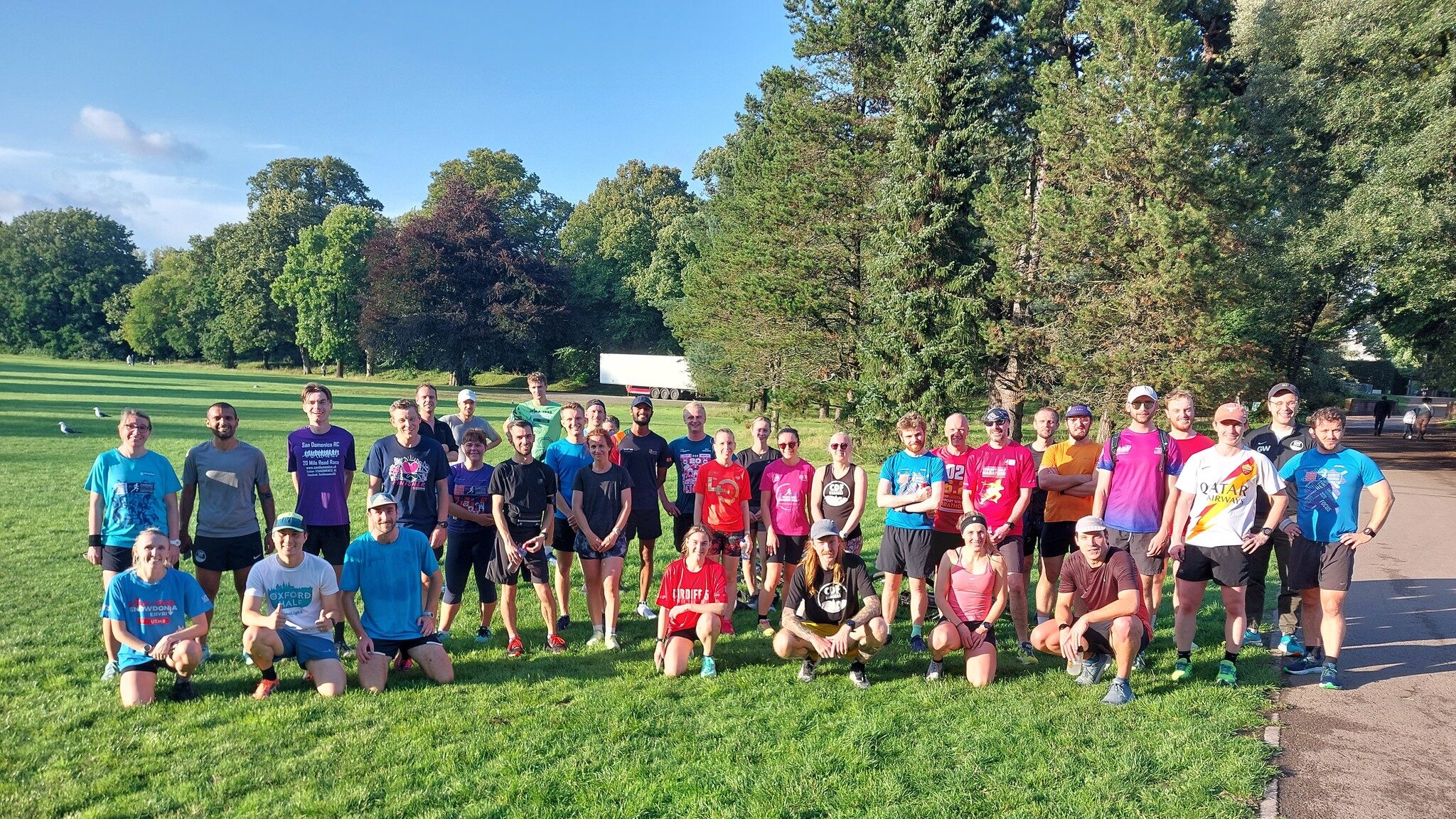 A large group of runners posing for a photo after a session in the park on a sunny day.