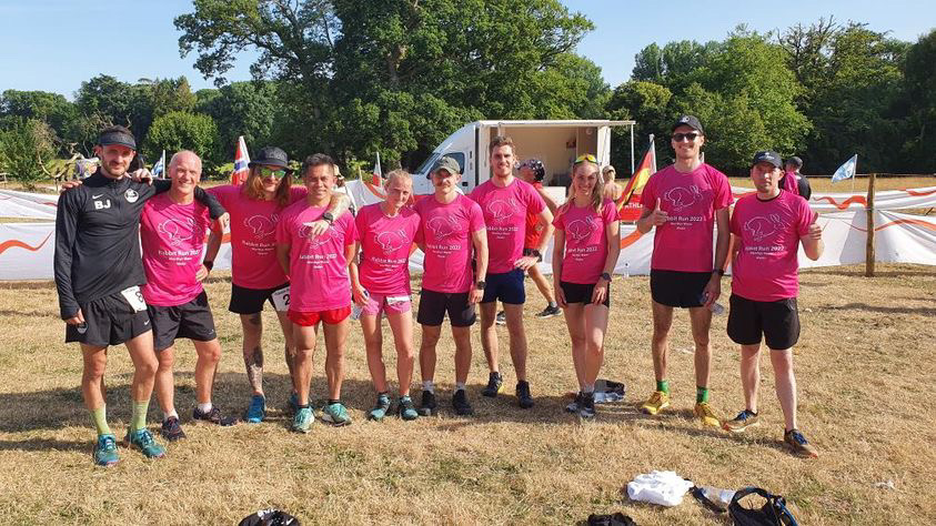 10 happy tired runners arm in arm in matching race finisher t-shirts after a race.