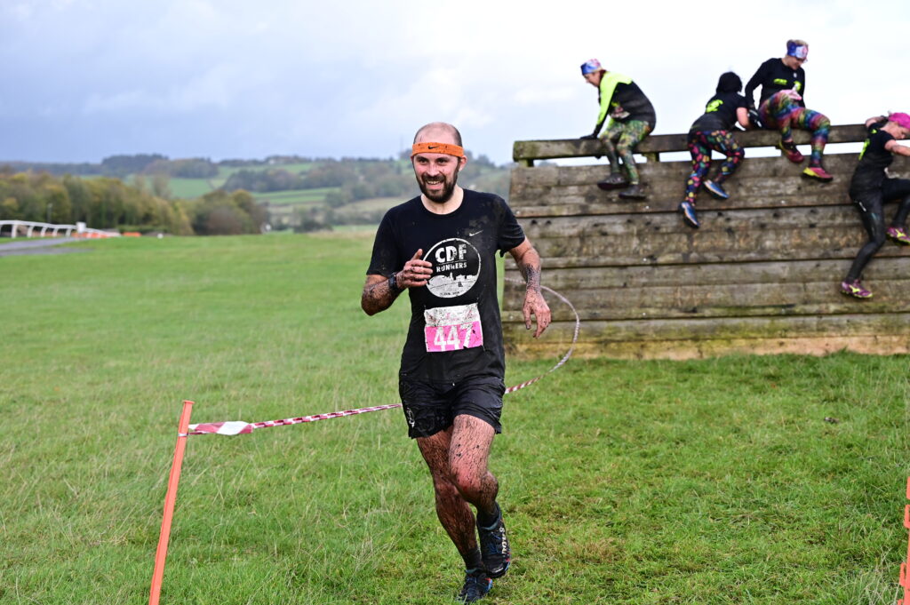 Stewart running covered head to toe in mud, with a climbing wall in the background.