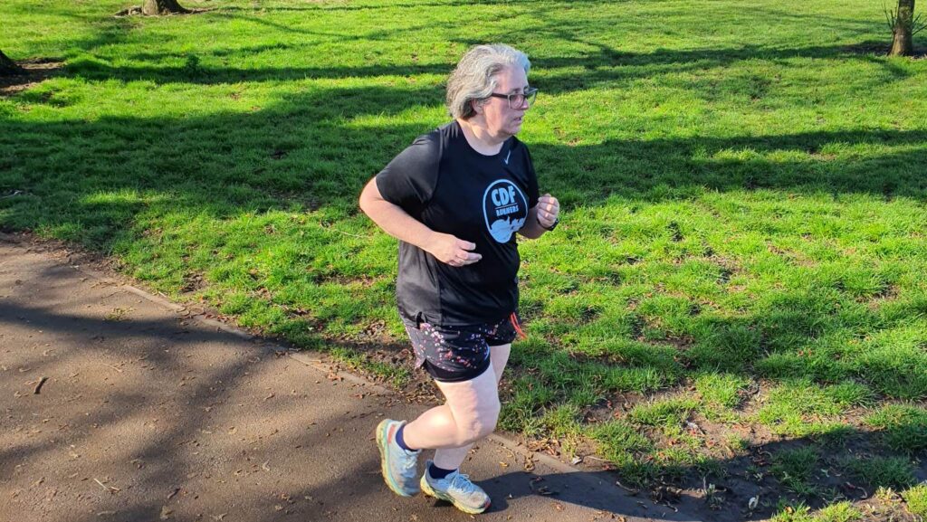 Side view of Charlotte running on a tarmac path with grass behind, looking resplendent in her black DF tshirt.